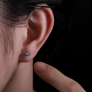 Close-up of a blue round stone earring with a three-claw silver setting on the ear