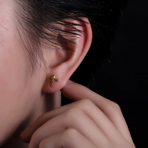 Detail of gold rose and dagger earring with zircon inlay worn on earlobe by a model