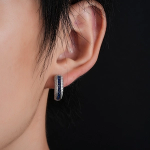Silver huggie hoop earrings with blue square gems and pave white zircons on a model