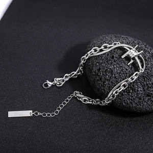 Detail of silver double-layered chain bracelet with industrial barbed wire charm on lava rock
