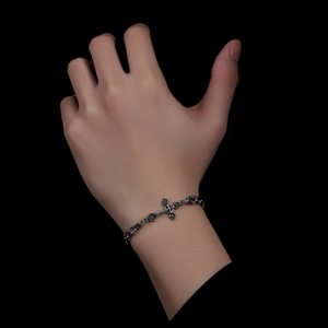 Gros plan d'un bracelet croix gothique vintage en argent porté sur un fond noir