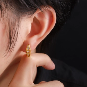 Macro shot of geometric gold earrings with three sparkling inlaid zircons on ear lobe