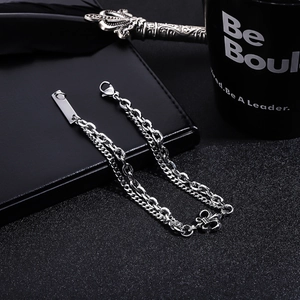 Detail eines silbernen doppellagigen Kettenarmbands mit Kreuzanhänger auf schwarzem Leder