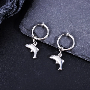Gros plan de boucles d'oreilles dauphin en acier inoxydable poli sur fond de pierre