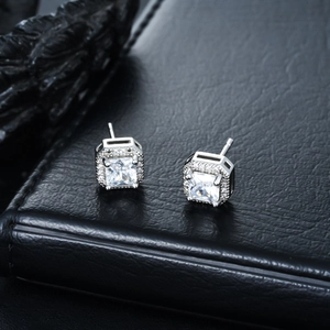 Macro shot of silver square cubic zirconia stud earrings with halo setting on leather