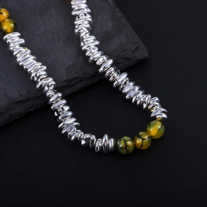 Detail of metallic beads and green agate stone necklace on dark textured stone
