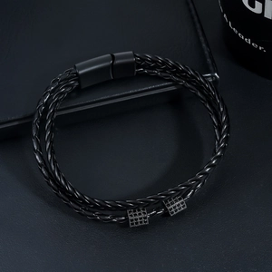 Detail of woven black leather bracelet with magnetic clasp and square patterned charms