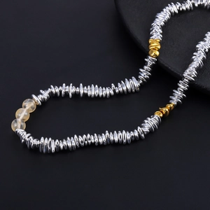 Minimalist silver disc and yellow bead necklace on a textured black stone display