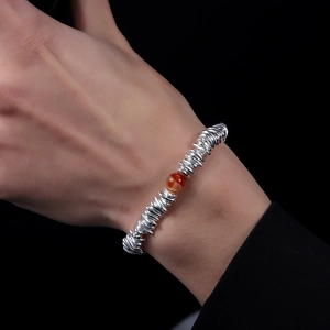 Close-up of silver spiral link bracelet with a red agate bead on a person's wrist