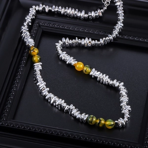 Silver metallic beads and amber resin stone necklace on a dark textured background