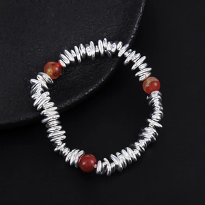 Macro detail of beaded silver bracelet with red agate accents on natural black stone plate