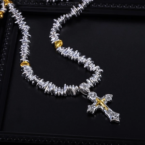 Macro shot of punk cross pendant with textured silver and gold beads on a black tray