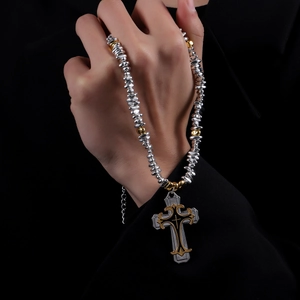 Détail du pendentif croix avec perles métalliques argentées et textures dorées chic