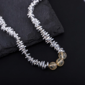 Close-up of irregular silver metal beads and yellow gemstone beads on a textured stone