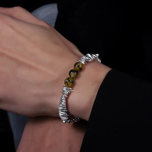 Detail of silver twisted metal bracelet featuring green patterned beads on wrist