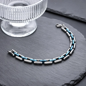 Silver and blue stainless steel link bracelet with lobster clasp on dark stone pedestal