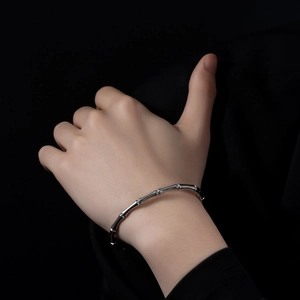 Detailed view of silver bamboo joint stainless steel bracelet on wrist with dark background