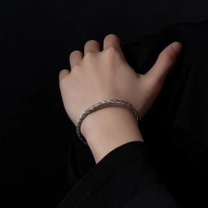 Detail of silver woven texture cuff bracelet on wrist against dark suit background