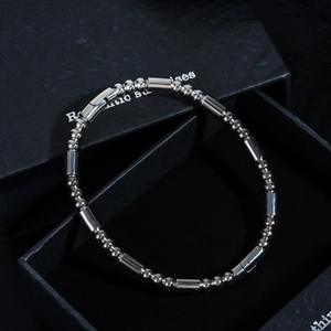 Détail d'un bracelet en perles d'acier argenté poli posé sur un coffret cadeau noir élégant