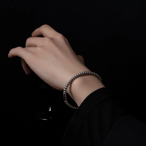 Detailed view of a polished stainless steel beaded bracelet with cylindrical clasp on wrist