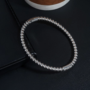 Polished silver beaded bracelet with cylindrical clasp on a premium black leather surface