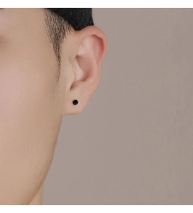 Close-up of minimalist black round stud earring worn on ear with clean matte finish