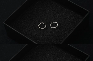 Gros plan de boucles d'oreilles créoles argentées texturées dans un écrin noir
