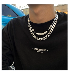 Close-up of men's layered silver cuban link chain and pearl necklace on black shirt