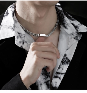 Close-up of polished silver Cuban chain with flat rectangular pendant on model neck