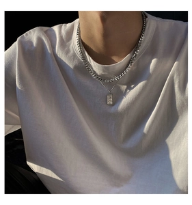 Detail of layered silver Cuban chain and rectangular relief pendant on a white T-shirt