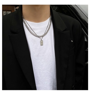 Detail shot of a double-layered silver necklace with cuban links and a rectangular pendant