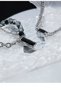 Gros plan du collier avec pendentif en onyx noir et chaîne perlée sur verre texturé