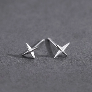 Vue macro de boucles d'oreilles étoile à quatre branches en argent sur fond sombre texturé
