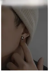Close-up of cross stud earring with four black square stones on male model ear