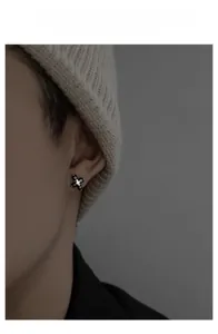 Close-up of cross stud earring in black and silver metal worn with a beanie hat