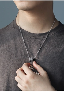 Close-up of a vintage silver cylinder pendant with intricate dragon engravings on a male model