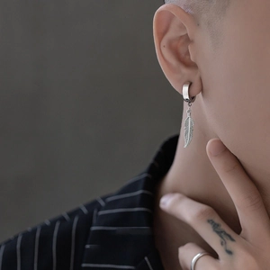 Détail d'un pendant d'oreille plume en titane argenté sur un mannequin au style urbain