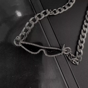 Detail of silver Cuban chain necklace with stone-studded black sunglasses pendant