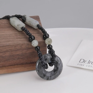 Dettaglio macro di un ciondolo Pingan Kou in pietra vintage con collana di perle su legno