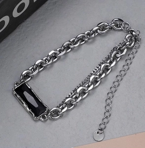 Gros plan d'un bracelet à chaînes argentées superposées avec une pierre noire taillée