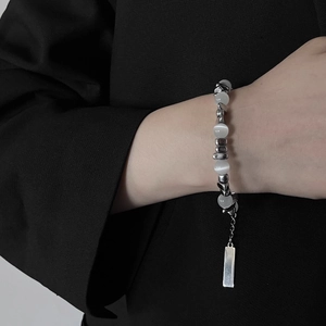Détail d'un bracelet en opale et perles argentées porté sur fond de costume noir chic