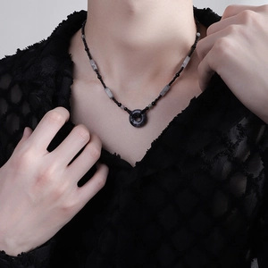 Dettaglio della collana hip-hop retrò con perline scure e ciondolo ad anello grigio su mesh