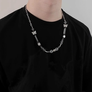 Détail du collier de perles avec pendentif papillon et dés porté sur un t-shirt noir