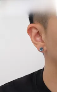 Nahaufnahme eines silbernen Herrenohrsteckers mit blauem Topas am Ohr des Models