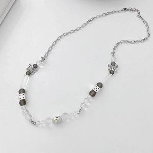 Détail du collier de perles avec motifs papillons argentés et pendentifs dés sur fond blanc