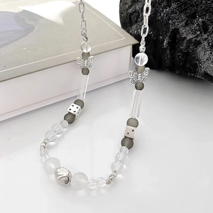 Détail du collier de perles avec breloques papillon et dés sur fond minimaliste