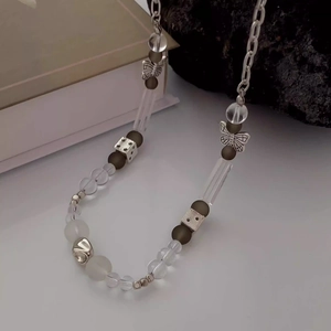 Détail du collier de perles avec pendentifs papillon, cœur et dés sur fond blanc