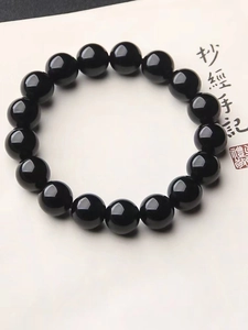 Gros plan d'un bracelet de perles en verre noir poli sur fond de calligraphie chinoise
