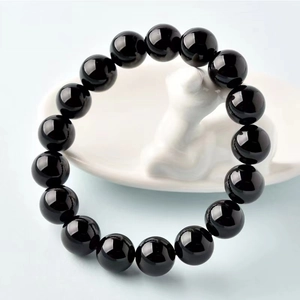 Gros plan de perles de verre noires polies sur un plateau blanc avec reflets de lumière
