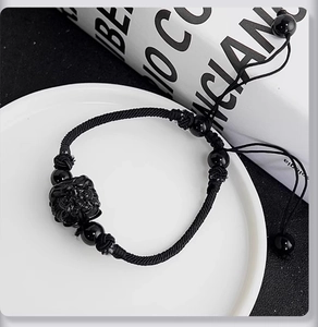 Macro shot of black woven bracelet with a carved Pixiu stone and adjustable pull cord